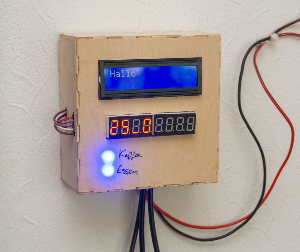 Holzkästchen an der Wand mit LCD-Anzeige „Hallo“, Ziffernanzeige und blauen LEDs für Kaffee und Essen
