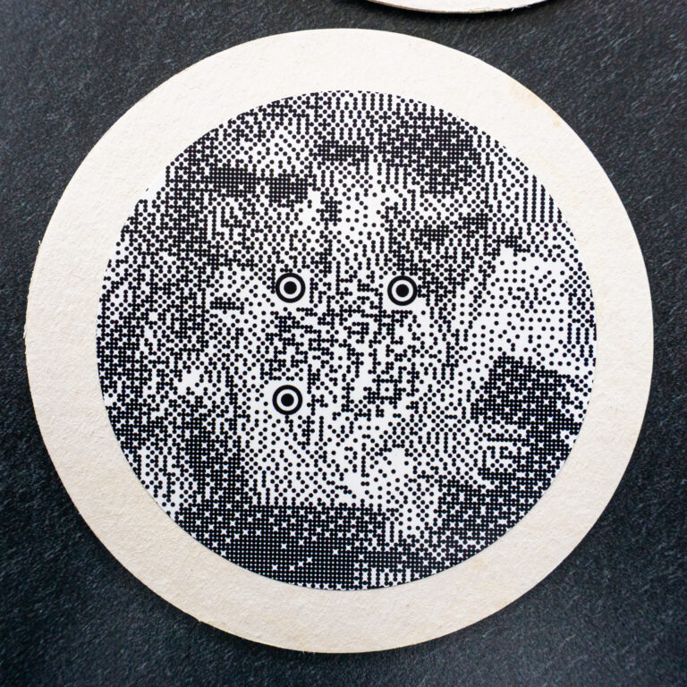 Runder Bierdeckel mit QR-Bild: ein Foto als Punktmuster, mittendrin ein lesbarer QR-Code mit runden Markierungen